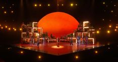 the stage is lit up with bright lights and people standing on it in front of an orange ball