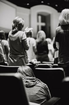 black and white photograph of people in an auditorium watching something on the screen with their hands up