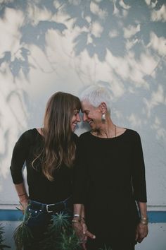 two women standing next to each other in front of a tree