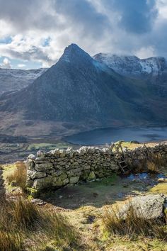 a stone wall in the middle of a mountain range with snow on the mountains behind it