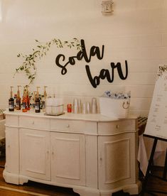 a bar with bottles and glasses sitting on top of it next to a sign that says soda bar