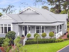 a grey house with white trim on the front and side of it, surrounded by trees