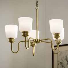 a brass chandelier with three white glass shades hanging from it's arms