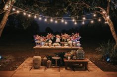 a wooden table topped with lots of cake and desserts next to lights strung from trees