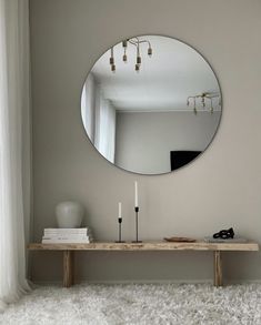 a mirror on the wall above a wooden table with two candles and a vase next to it