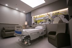 a hospital room with a bed, chair and wall mural on the wall behind it