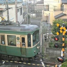 a green train traveling down tracks next to a traffic light and street signs on the side of a road