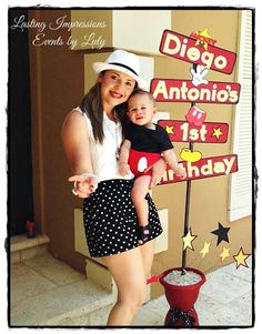 a woman holding a baby in front of a sign that says diego and antonio's 1st birthday