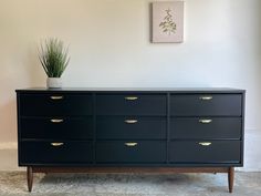 a large black dresser with gold handles and drawers in a white room next to a potted plant