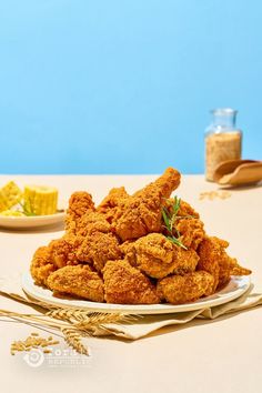 fried chicken is piled on a plate next to corn and seasoning in a glass jar