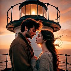 a man and woman standing next to each other near a light house at the ocean