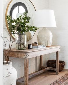 a table with a mirror, lamp and vase on it in front of a white brick wall