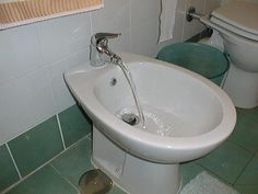 a white toilet sitting next to a bidet in a bathroom under a faucet