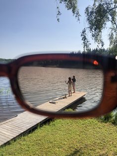 two people standing on a dock in front of a pair of glasses that are reflecting them