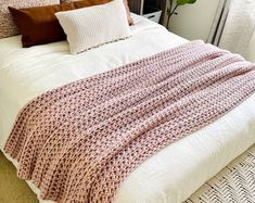 a bed with a blanket on top of it next to two pillows and a potted plant