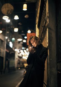 a woman leaning against a wall while looking at her cell phone in an alleyway