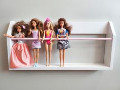 five barbie dolls are lined up on a shelf in a playroom or dollhouse