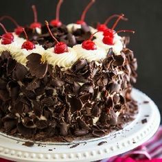 a close up of a cake on a plate with cherries and chocolate shavings