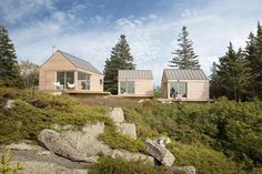 two small wooden houses sitting on top of a hill next to some rocks and trees