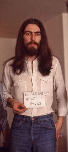 a man with long hair and beard holding a paper sign in his hand that says we are not these bodies