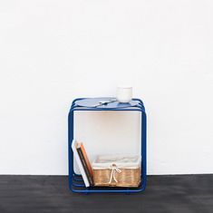 a basket with books and a cup on it sitting in front of a white wall