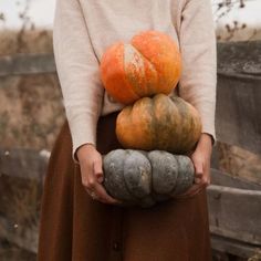 a woman holding three pumpkins in her hands