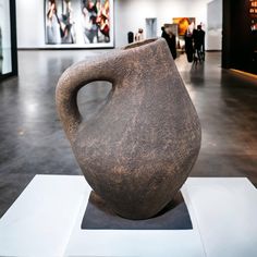 a large brown vase sitting on top of a white pedestal in a room filled with people