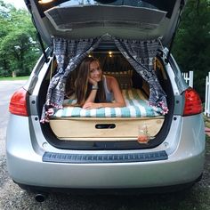 a woman laying in the back of a car with her bed on it's trunk