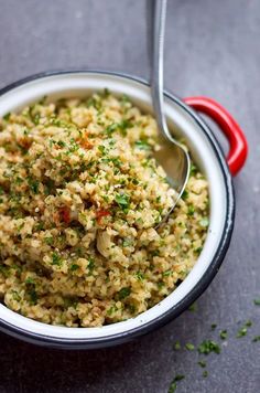 a bowl filled with rice and vegetables on top of a gray table next to a red spoon