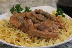 a white plate topped with pasta and meat covered in gravy on top of a marble counter