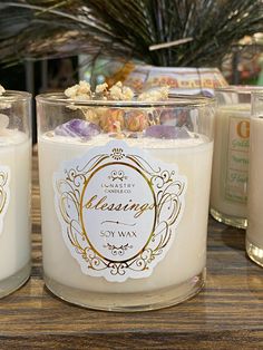 three candles sitting on top of a wooden table next to each other with labels in front of them