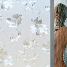 a woman standing in front of a shower next to a window with flowers on it