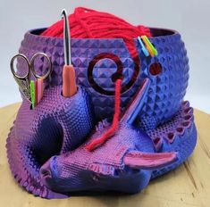 a purple basket with scissors, yarn and other crafting items in it on a wooden table