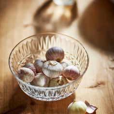 a glass bowl filled with garlic on top of a wooden table