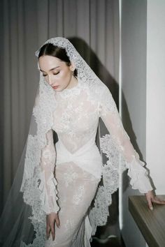 a woman in a white wedding dress with a veil on her head is leaning against a window sill