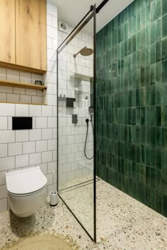 a white toilet sitting next to a shower in a bathroom with green tiles on the walls