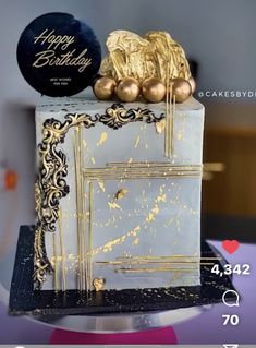 the cake is decorated with gold and black icing, along with two golden balloons