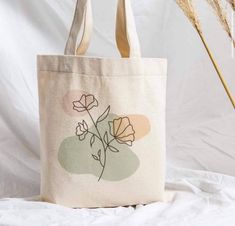 a tote bag sitting on top of a bed next to some dried grass and a plant