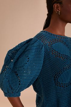 a woman wearing a blue top with crochet details on the sleeves and shoulders