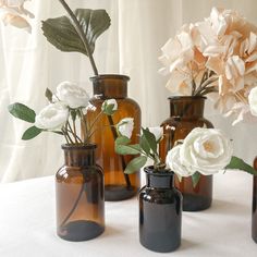 three brown vases with white flowers in them on a tablecloth covered table cloth