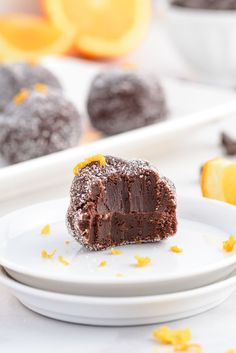 a piece of chocolate cake on a white plate with oranges in the back ground