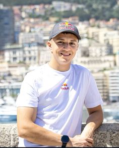 a young man wearing a hat and white shirt sitting on a ledge in front of a city