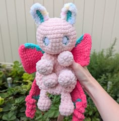 a pink crocheted stuffed animal with blue eyes holding it's tail in the air