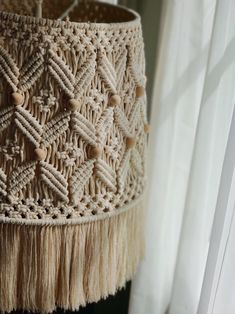 a woven lamp shade with tassels hanging from it's sides on a window sill