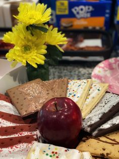 an apple and some crackers are on a plate with flowers in the back ground