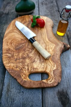 a wooden cutting board with a knife on top of it next to some olive oil and tomatoes