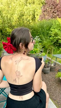 a woman sitting on top of a wooden table next to a green plant filled garden