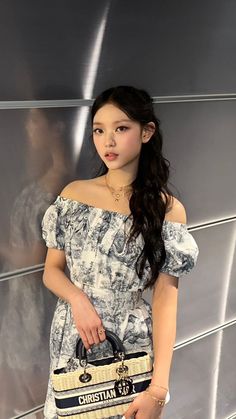 a young woman holding a purse standing in front of a wall