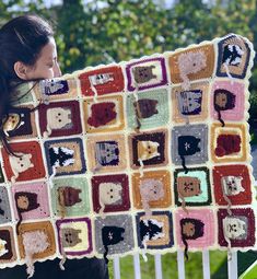 a woman holding up a crocheted blanket with cats and dogs in squares on it