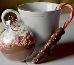 two candy canes in a glass ornament next to a mug filled with marshmallows